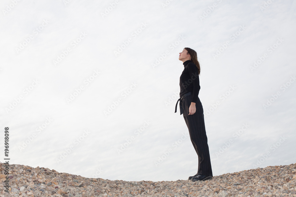 lone young woman standing on pebbles and enjoying the sun lone young woman standing on pebbles and enjoying the sun