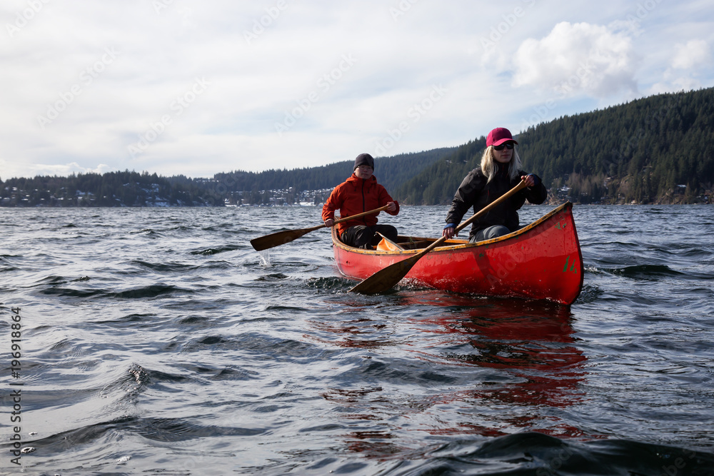 Fototapeta premium Couple friends on a wooden canoe are paddling in an inlet surrounded by Canadian mountains. Taken in Indian Arm, near Deep Cove, North Vancouver, British Columbia, Canada.