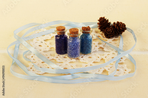 Three tiny glass bottles with a cork stopper, filled with a blue colours of beads, white knitted napkin and blue ribbon for decoration on a beige background. three lumps of larch photo