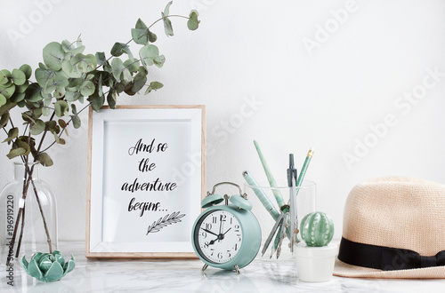 Poster framewith tiped text: Adventure begins, front view, with decor elements and female accessories, flowers and blank copy space over the white wall. photo