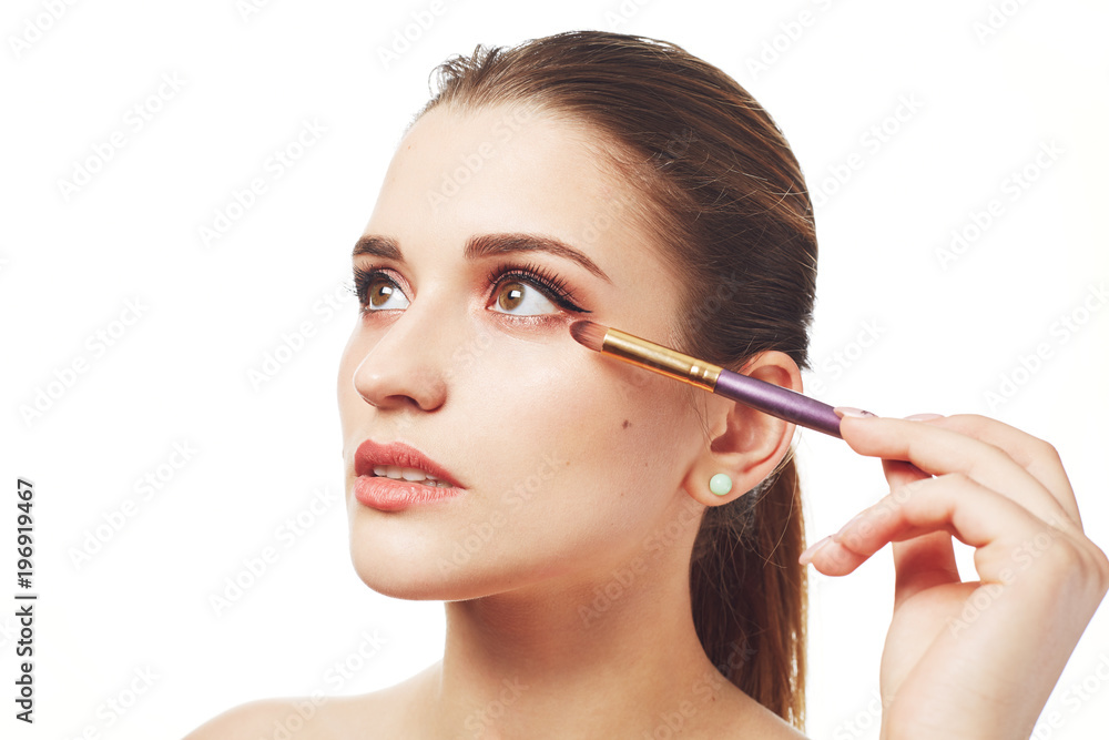 Photo of adorable woman does make up with special brush, has healthy pure skin and painted lips, being professional make up artist, isolated over white background. People and beauty concept.
