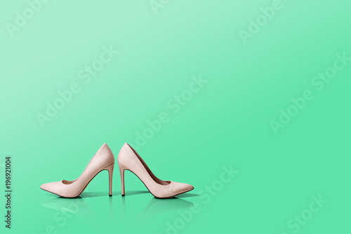 Beige high heels isolated on a green pastel background. Reflection of shoes. High heels stand next to each other, beige and shiny. The concept of fashion, online store, sale of clothes, shoes.
