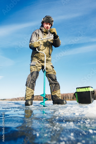 fisherman with auger in winter ice fishing photo