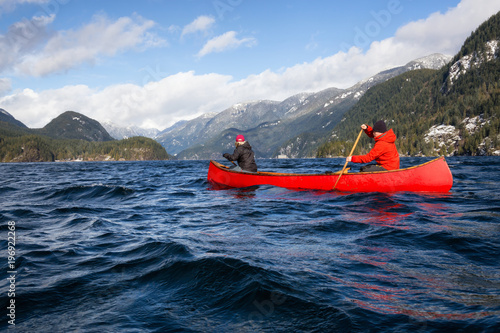 Fototapeta Couple friends on a wooden canoe are paddling in an inlet surrounded by Canadian mountains