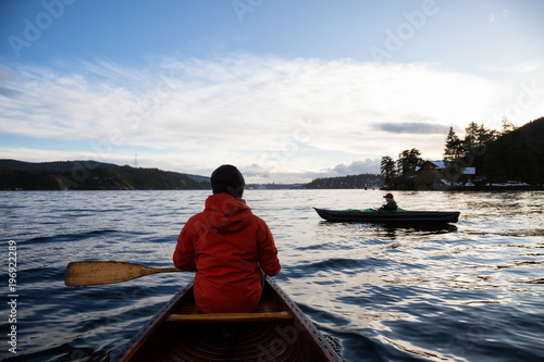 Man on a wooden canoe is paddling during a vibrant sunset. Taken in Indian Arm, North of Vancouver, British Columbia, Canada.