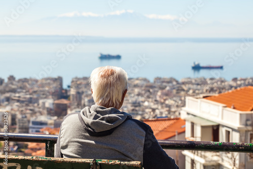 Old man sitting on a bench looking at the gulf in Thessaloniki, Greece