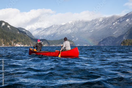 Couple friends on a wooden canoe are paddling in an inlet surrounded by Canadian mountains. Taken in Indian Arm, near Deep Cove, North Vancouver, British Columbia, Canada.