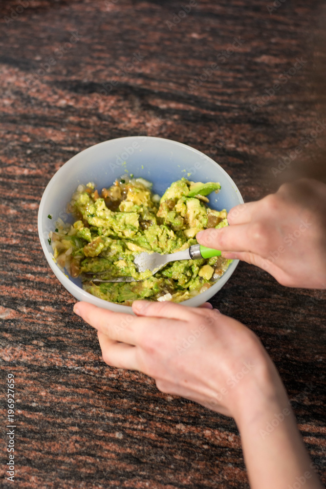 Cooking traditional latin american mexican sauce guacamole in a bowl with avocado, making guacamole in the kitchen, guacamole recipe