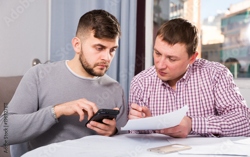 Serious males with documents and phone at home table
