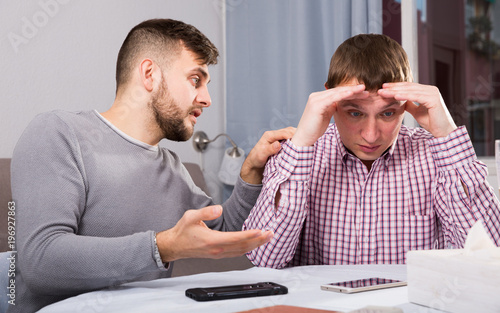 Friend soothing upset man at home table