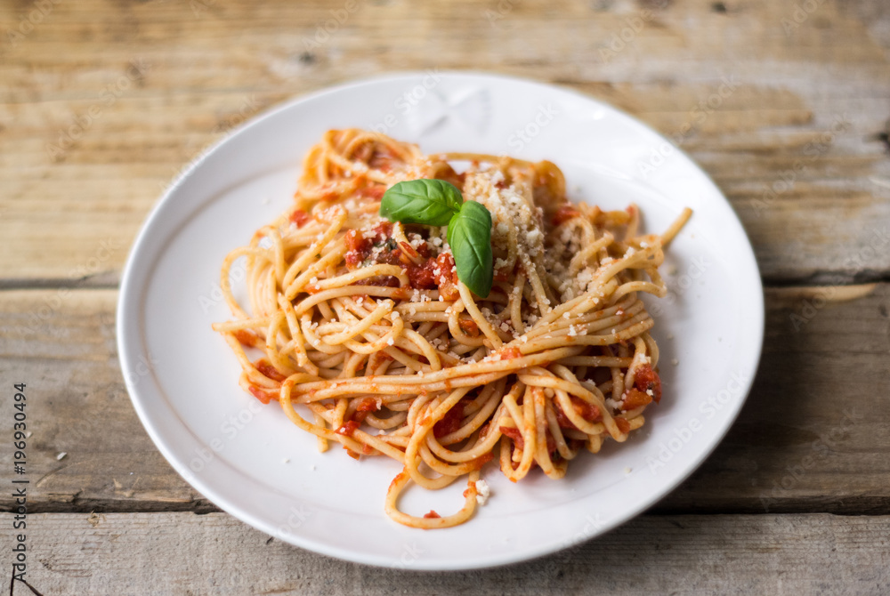 Homemade Italian pasta spaghetti with tomato sauce, fresh herbs and grated parmesan cheese on wooden rustic table