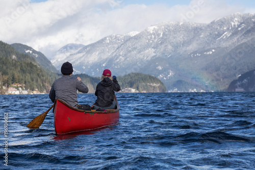 Couple canoeing on a wooden canoe in a beautiful Canadian Mountain Landscape during a vibrant winter day. Taken in Indian Arm, Vancouver, British Columbia, Canada.