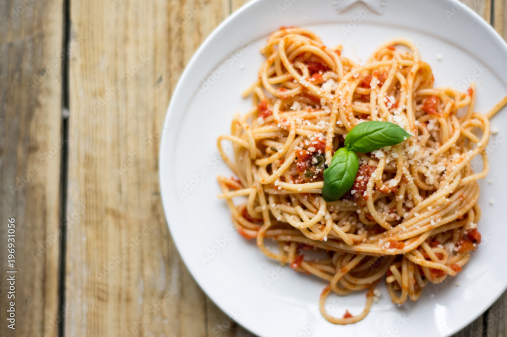 Homemade Italian pasta spaghetti with tomato sauce, fresh herbs and grated parmesan cheese on wooden rustic table