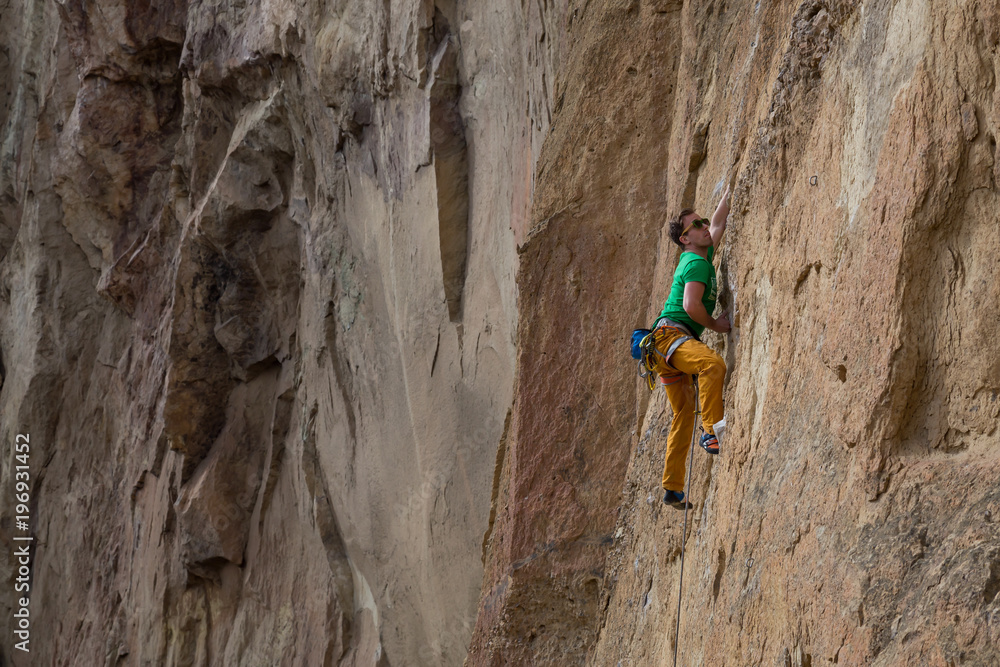 Adventurous man is rock climbing on the side of a steep cliff during a cloudy winter evening. Taken in Smith Rock, Oregon, North America. Adventurous man is rock climbing on the side of a steep cliff during a cloudy winter evening. Taken in Smith Rock, Oregon, North America.