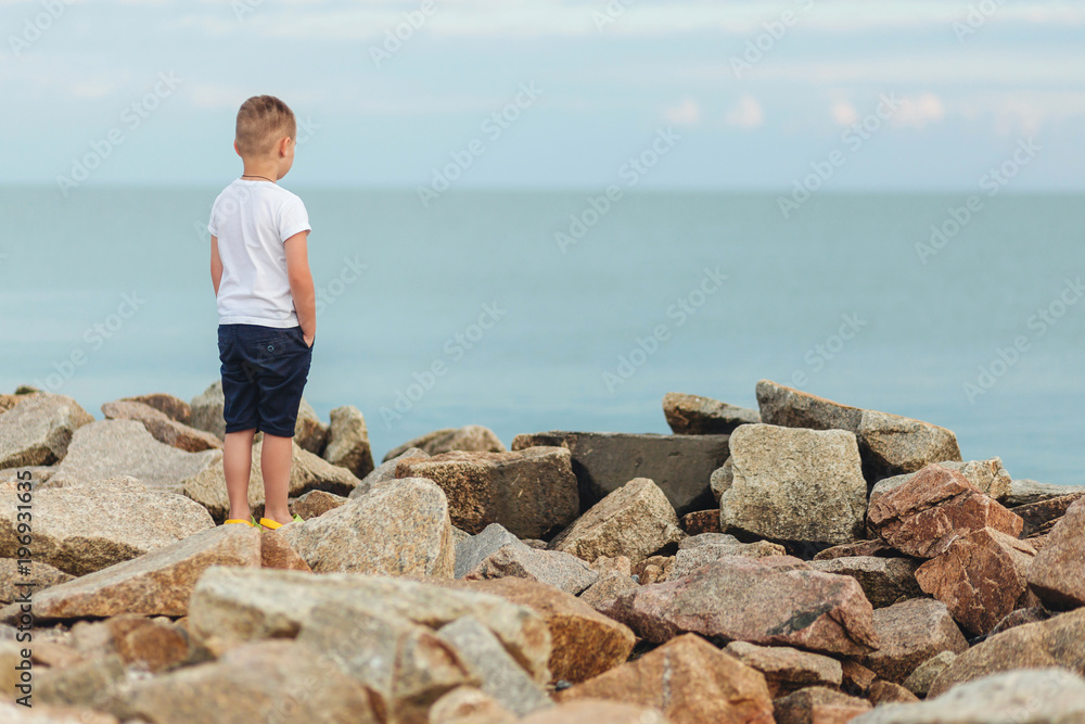 Little boy standing alone and looking at the beautiful ocean