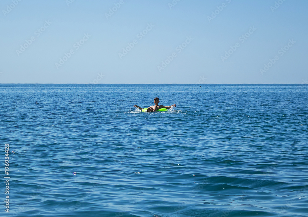 a young man swims on a large inflatable circle, on the sea