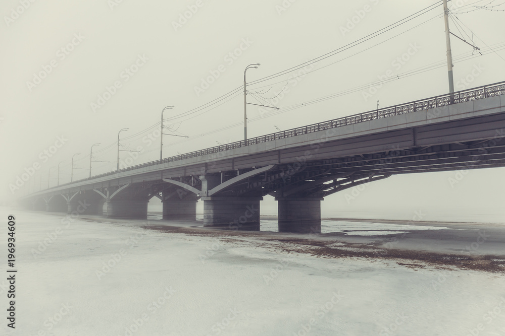 Bridge in fog over frozen river in ice and snow. Mysterious urban landscape in foggy day, vintage toned Bridge in fog over frozen river in ice and snow. Mysterious urban landscape in foggy day, vintage toned