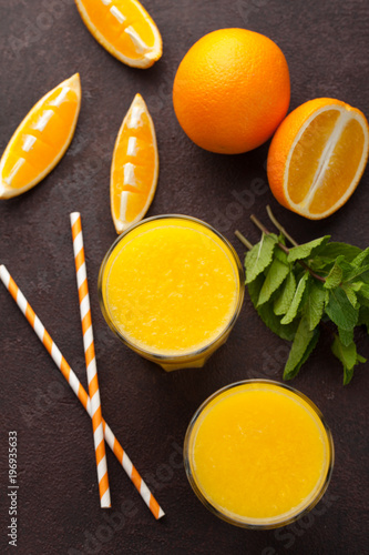 Two glasses of freshly squeezed orange juice and mint on a dark brown background. Top view