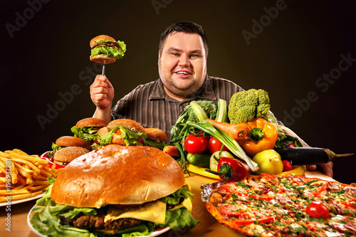 Diet fat man who makes choice between healthy and unhealthy food. Overweight male with hamburgers, french fries. Health problems due to malnutrition.