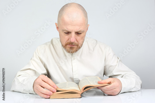 bald, bearded man in bright clothes reading a book of the Bible.