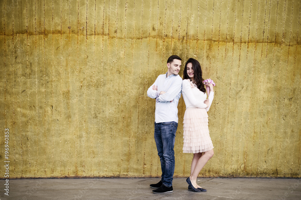 Young couple standing back to back simple golden background Young couple standing back to back simple golden background