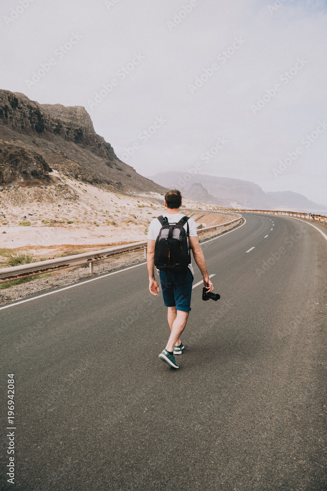 Traveler walks in the center of an epic winding road. Huge volcanic mountains in the distance behind him. Sao Vicente Cape Verde