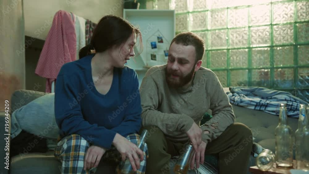 Smiling alcoholic young poor couple drink beer sit on sofa stress unhealthy creepy home desperate depressed unhappy adult alcoholism problem upset cheers tired slow motion portrait close up