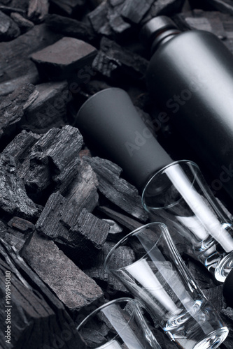 Black set of matte bottle of alcohol and shot glasses. On charcoal background. Black edition.Creative.Let's drink.Cheers.Mockup.Creative background of glass and charcoal