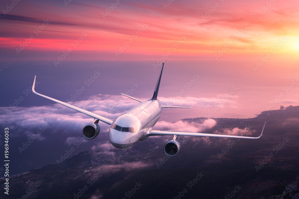 Naklejka premium Passenger airplane. Landscape with big white airplane is flying in the red sky over the clouds and sea at colorful sunset. Passenger aircraft is landing. Business trip. Commercial plane.Travel. Aerial