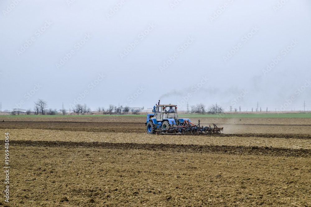 Fototapeta premium Lush and loosen the soil on the field before sowing. The tractor plows a field with a plow