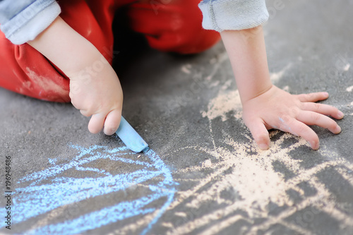 Closeup photo of little kid boy drawing with colored chalk on asphalt.