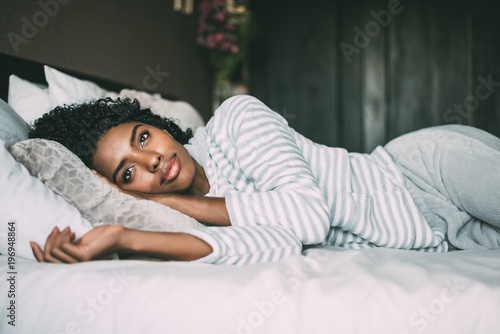 close up of a pretty black woman with curly hair smiling and lying on bed looking away