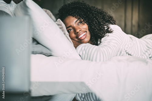 close up of a pretty black woman with curly hair smiling and lying on bed looking away