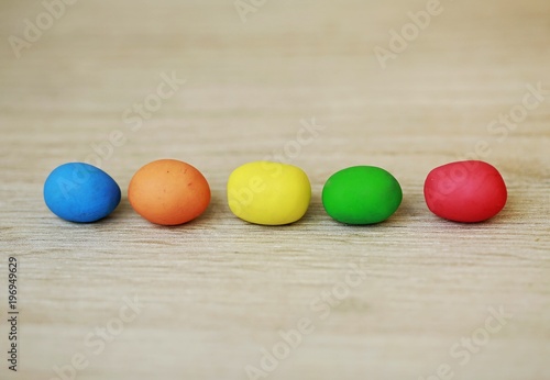 Colorful bright Easter little eggs lined up in the middle of picture, made of plasticine on wooden blurry background with blue, orange, yellow, green and red colors, contrast