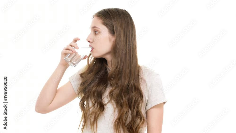 Portrait of good-looking teenage girl with brown hair being dehydrated and drinking mineral water from transparent glass, over white background closeup. Concept of emotions Portrait of good-looking teenage girl with brown hair being dehydrated and drinking mineral water from transparent glass, over white background closeup. Concept of emotions
