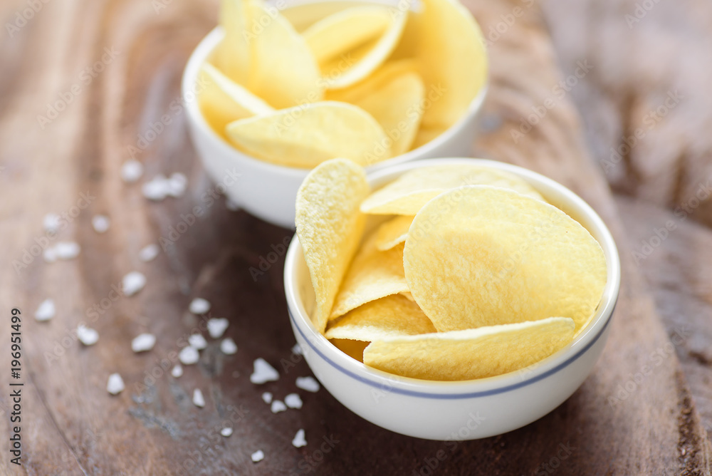 Potato chips in a bowl and salt on wooden background Potato chips in a bowl and salt on wooden background