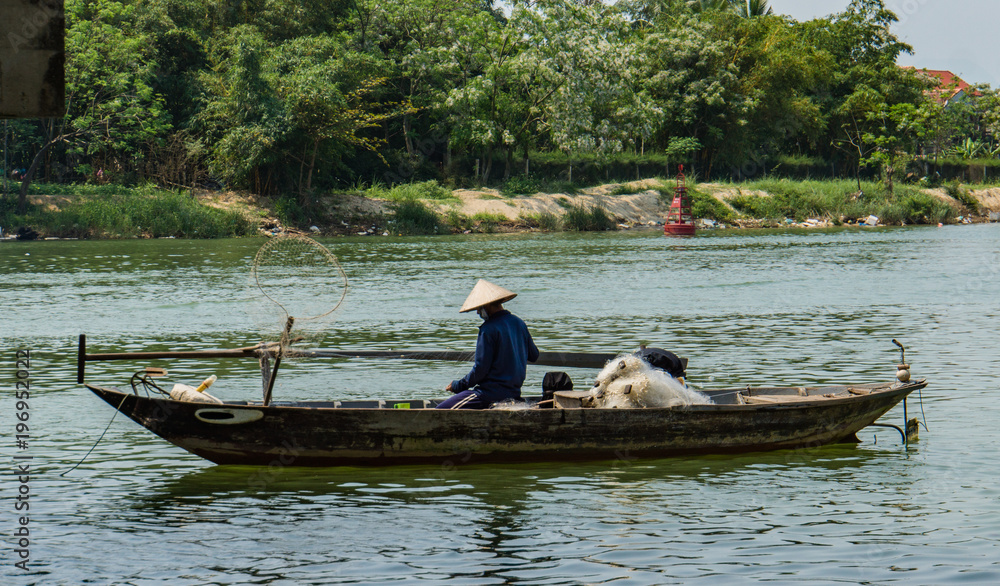 fisherman in boat pulling up his delicate fishing net  from the river bottom