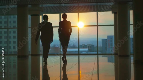The man and woman walking in the office hall on a sunset background. slow motion