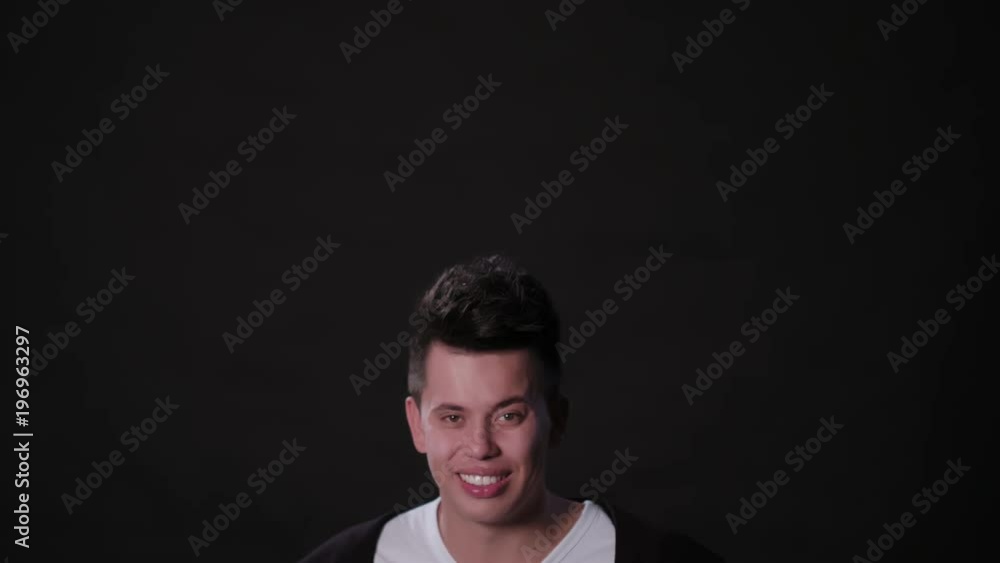 A young man smiling and standing and pointing his fingers upwards against a black background. Close-up shot A young man smiling and standing and pointing his fingers upwards against a black background. Close-up shot