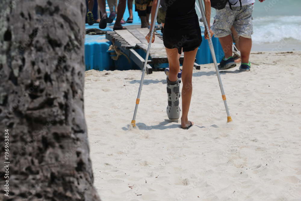 Accident tourist girl are walking up by crutches to the floating pier on the beach Accident tourist girl are walking up by crutches to the floating pier on the beach