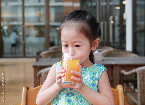 asian child girl drinking Orange juice at restaurant.