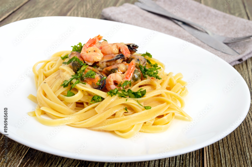 Pasta tagliatelle with seafood and cream sauce on a white plate on a wooden table.