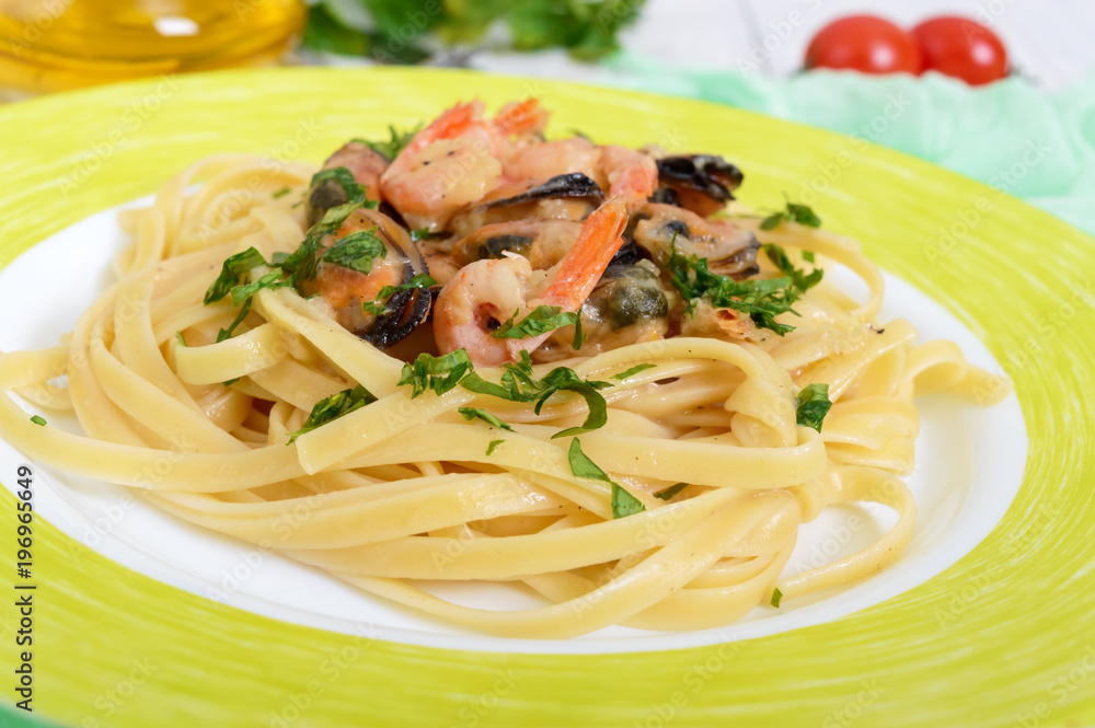 Pasta tagliatelle with seafood and cream sauce on a plate on a white wooden background.