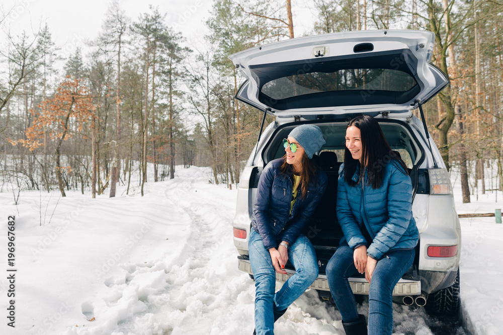 Two cheerful women travel by car in winter. Travel background
