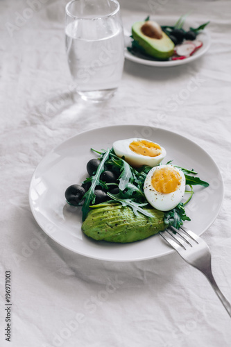 Healthy salad with arugula, avocado, egg and olives