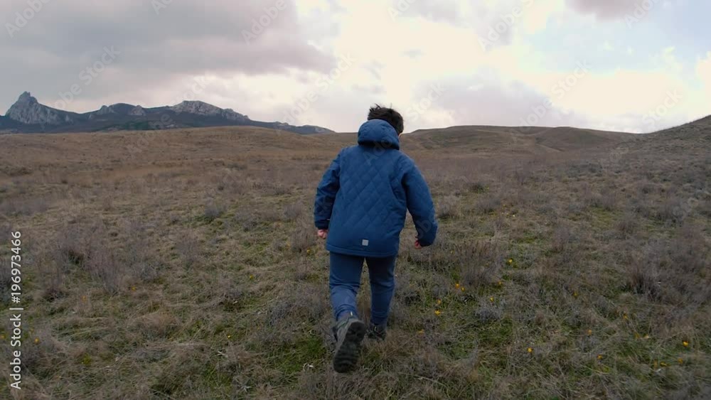 A boy on field with yellow flowers run to horizon with rocks. Slow motion video A boy on field with yellow flowers run to horizon with rocks. Slow motion video