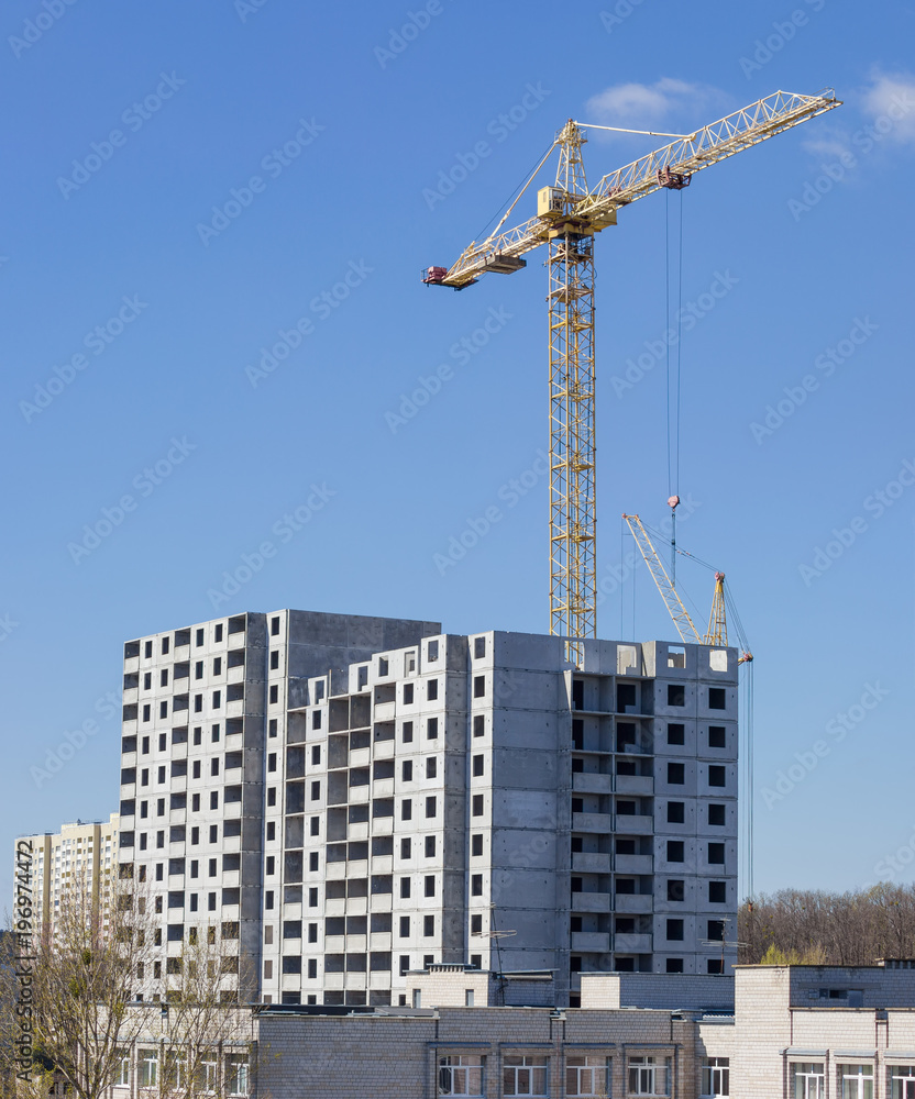 Multistory house under construction and tower crane against the sky