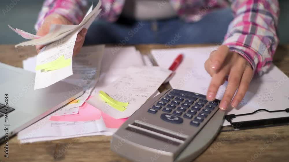 faceless anonymous woman hands working with bank paperwork bills and financial documents calculating monthly expenses and debt with calculator and laptop in domestic banking and finance accounting 