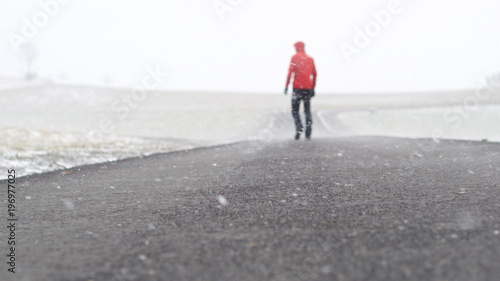 Person mit roter Jacke von hinten im Schneesturm, Schneefall