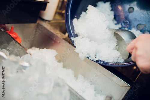 silver ice scoops in a large ice-filled bucket with blurred wine glasses in the background. Catering set-up ready for the event to begin. photo